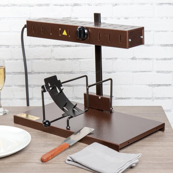A Bron Coucke cheese raclette machine on a wood table with a knife and plate.