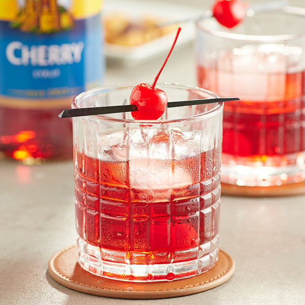 A glass of red liquid with a cherry on top and a toothpick in it.
