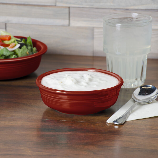A Scarlet Fiesta China bowl filled with yogurt on a table with a bowl of salad.