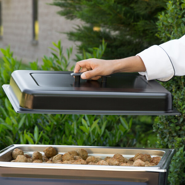 A person holding a black rectangular lid open over a tray of food.
