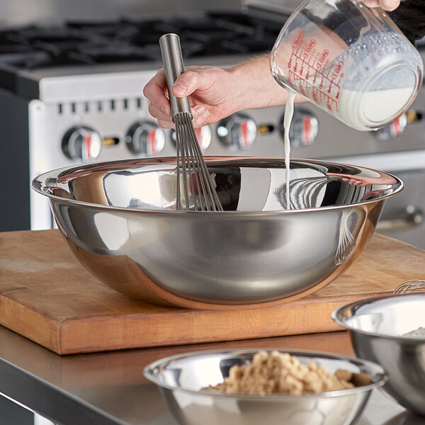 A person using a whisk in a large stainless steel mixing bowl.