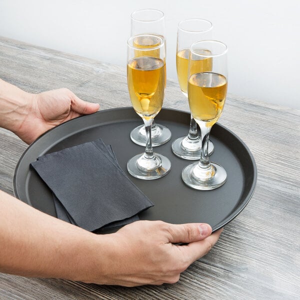 A person holding a Cambro non-skid serving tray with glasses of wine and napkins.