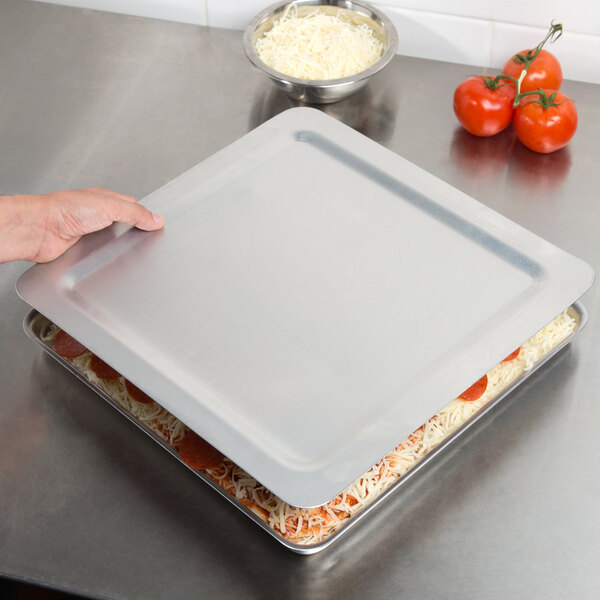 A person holding a tray of food with a square deep dish pizza pan lid on it.