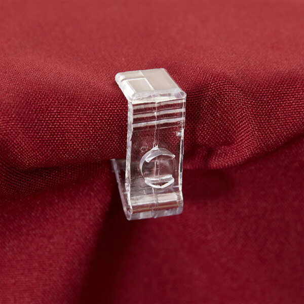 A clear plastic Snap Drape C skirt clip on a red fabric table.