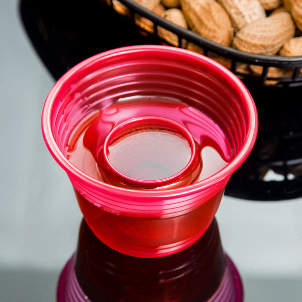 A red Fineline plastic cup filled with a red drink next to peanuts.