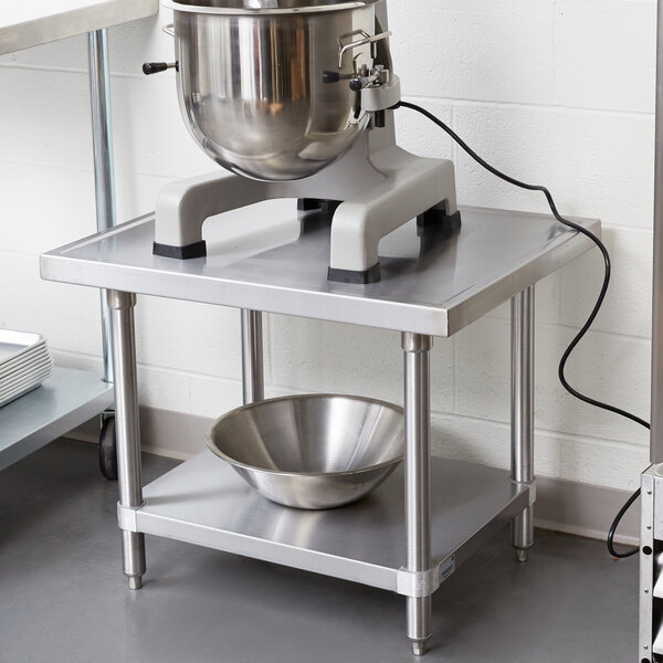 A stainless steel Advance Tabco mixer table with a mixer and a silver bowl on it.