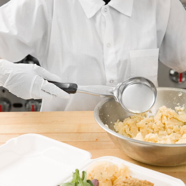 A person in a white shirt and gloves using a Vollrath black round spoodle to mix food in a bowl.