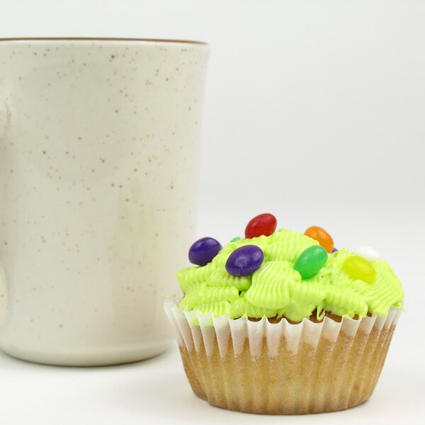 A white fluted baking cup with a cupcake and candy on top on a white surface.