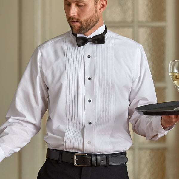 A man wearing a Henry Segal white tuxedo shirt with a wing tip collar and bow tie holding a tray with a glass of wine.