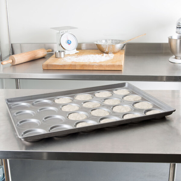 A Chicago Metallic baking tray with dough for hamburger buns in it on a counter.