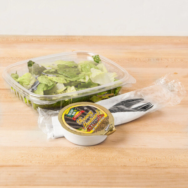 A Genpak clear plastic deli container of salad with lettuce and other food on a table.