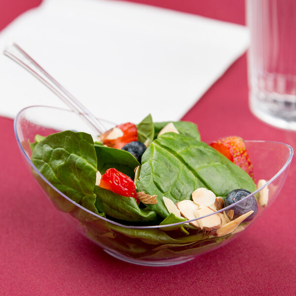 A bowl of salad with fruit and nuts in a clear plastic bowl on a table.