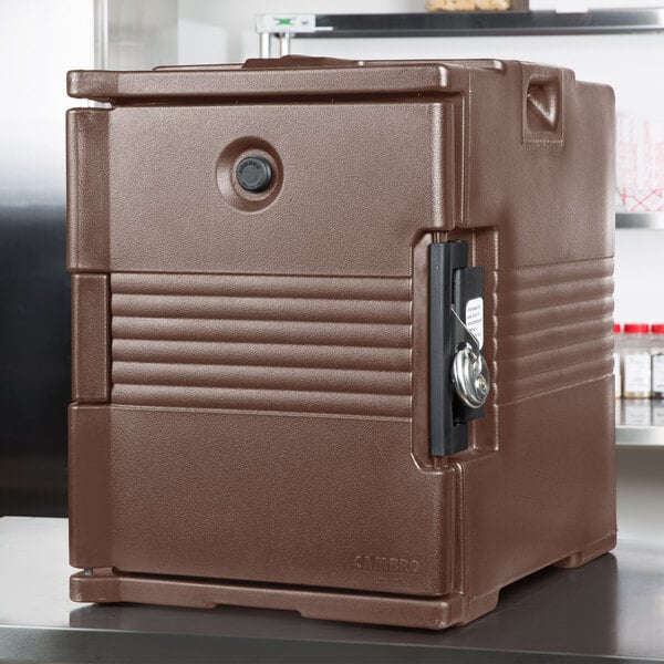 A dark brown Cambro front loading food pan carrier with a lock on the counter.