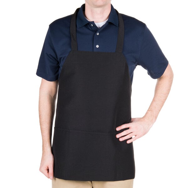 A man wearing a black Chef Revival bib apron with 3 pockets standing in a professional kitchen.