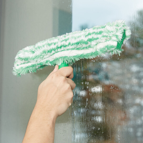 A hand cleaning a window with a Unger green and white StripWasher.