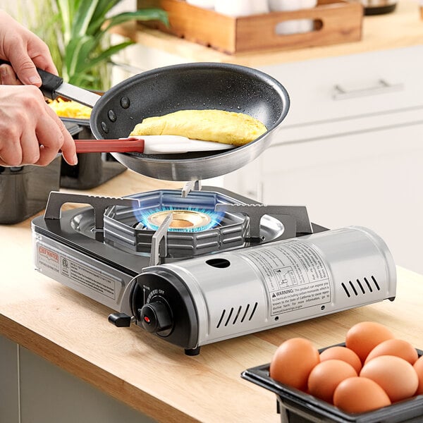 A person using a Chef Master 1-burner butane countertop range to cook eggs in a pan.