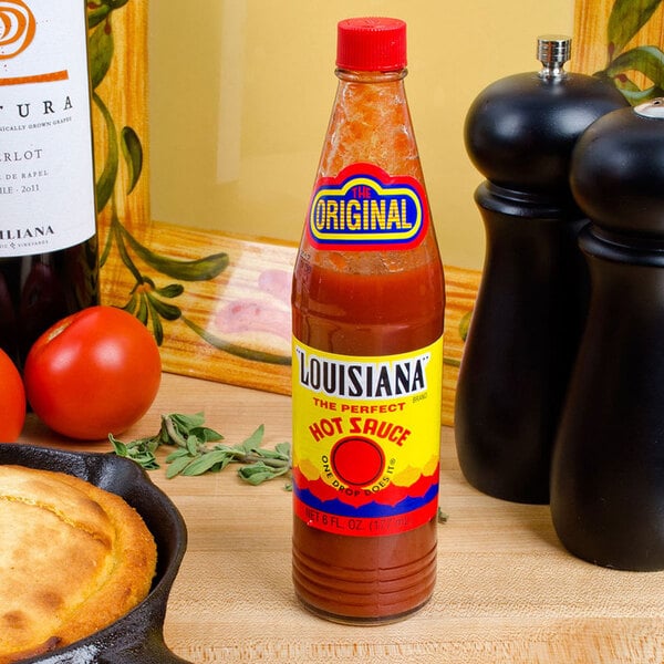A bottle of The Original Louisiana Brand hot sauce on a table with skillet cornbread and tomatoes.