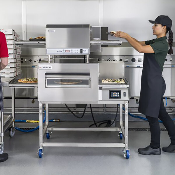A Lincoln Impinger conveyor oven with a pizza on the belt in a professional kitchen.