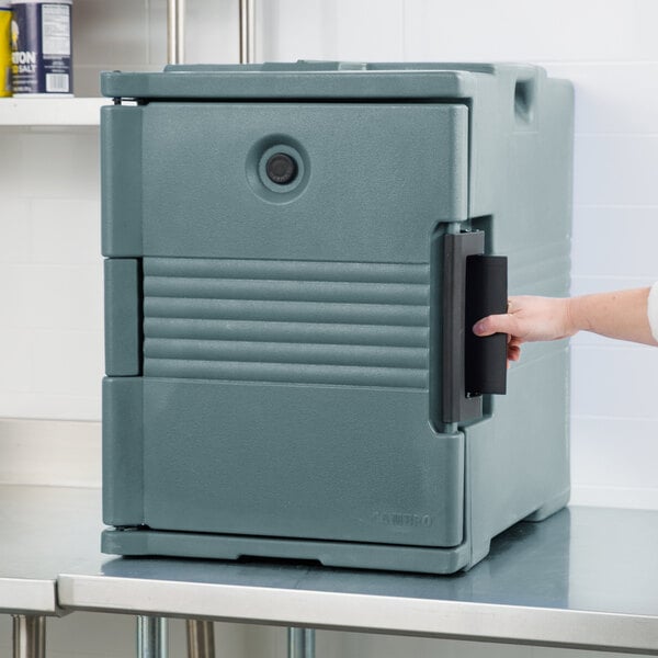A person opening a front-loading slate blue Cambro Ultra Pan Carrier on a counter.