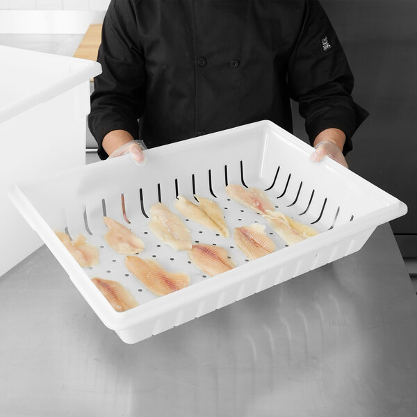 A person holding a Carlisle white deep drain tray with fish in it.