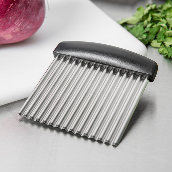 A black and silver Triangle Stainless Steel Crinkle Blade with a black handle on a counter with a piece of red onion.
