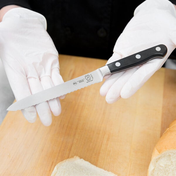 A person in white gloves uses a Mercer Culinary Renaissance tomato knife to cut bread.