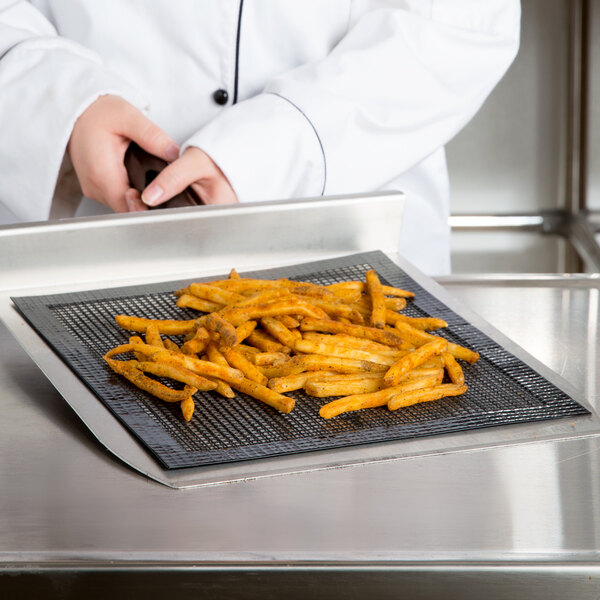 A person using a Baker's Mark mesh screen to cook french fries on a griddle.