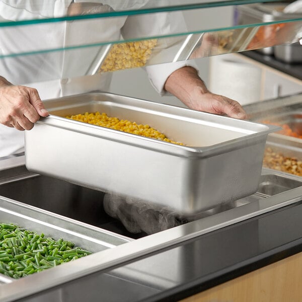 A person using a Choice stainless steel steam table pan to put food into a container.