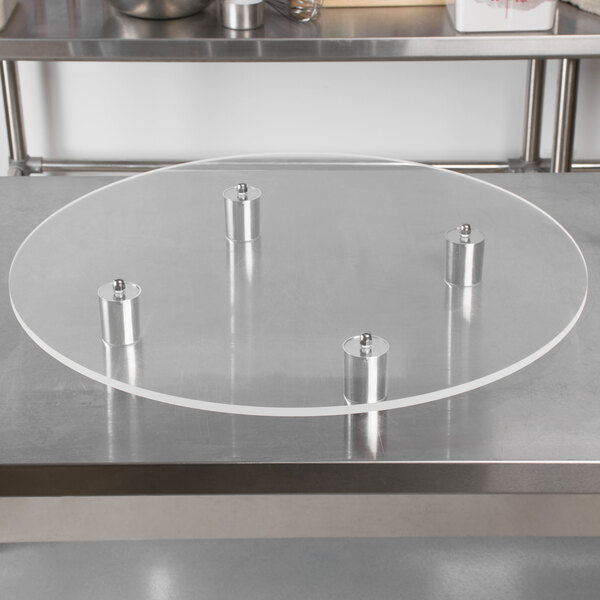 A round plexiglass cake stand on a metal table.
