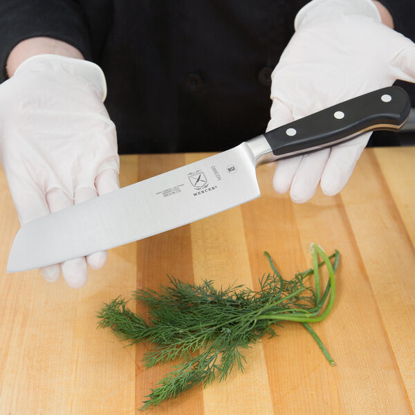 A person in gloves holding a Mercer Culinary Renaissance forged riveted Nakiri knife.