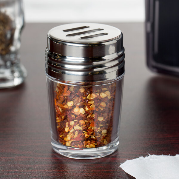 A clear glass American Metalcraft spice shaker with red pepper flakes.