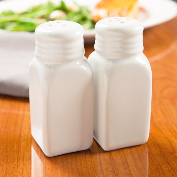 Two white ceramic American Metalcraft salt and pepper shakers on a table.
