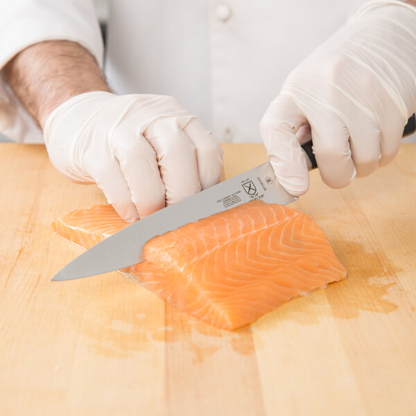 A person using a Mercer Culinary Z&#252;M 7" Forged Fillet Knife to cut a piece of salmon.