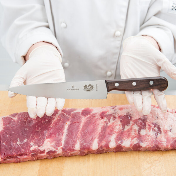 A person using a Victorinox serrated edge chef knife with a rosewood handle to cut meat.