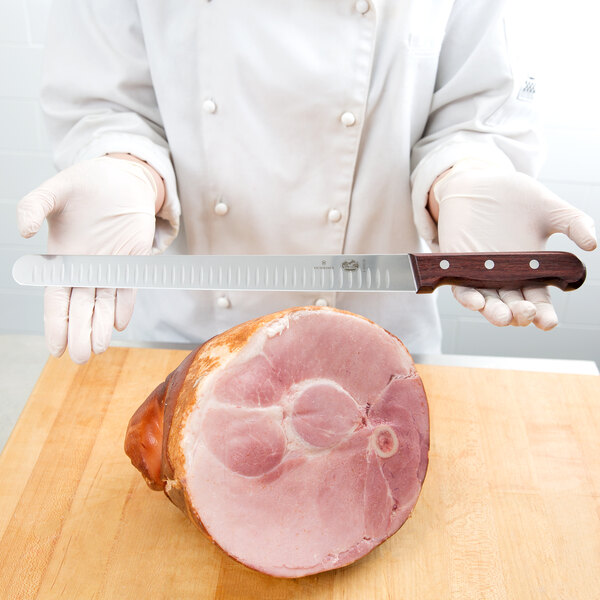 A person using a Victorinox Granton Edge Slicing / Carving Knife to slice ham.