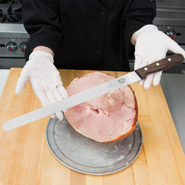 A person in white gloves using a Victorinox Rosewood Carving Knife to slice ham.