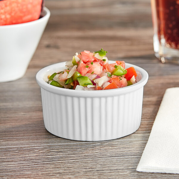 A bowl of salsa in a bright white fluted ramekin on a table.