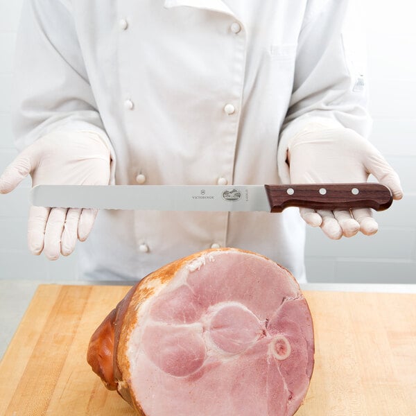 A chef using a Victorinox rosewood handled serrated carving knife to slice ham.