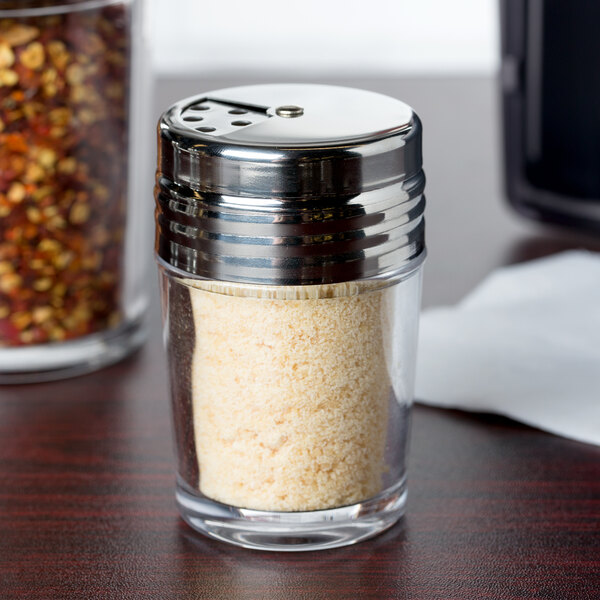 A clear glass American Metalcraft cheese shaker with a stainless steel lid filled with white powder.