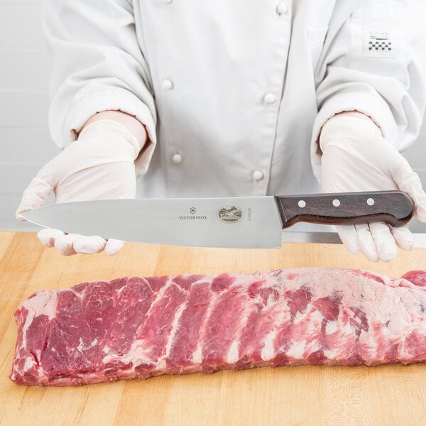 A person using a Victorinox 10" chef knife to cut meat on a wooden surface.