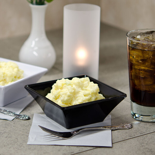 A bowl of mashed potatoes on a table with a glass of ice tea.
