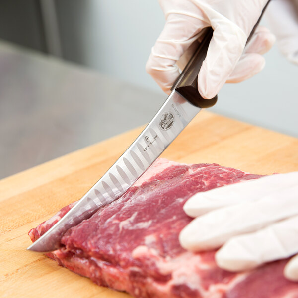 A person using a Victorinox curved boning knife to cut raw meat on a cutting board.