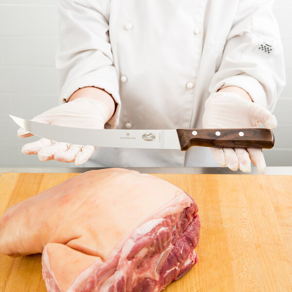 A chef using a Victorinox curved breaking knife to cut meat on a wooden surface.