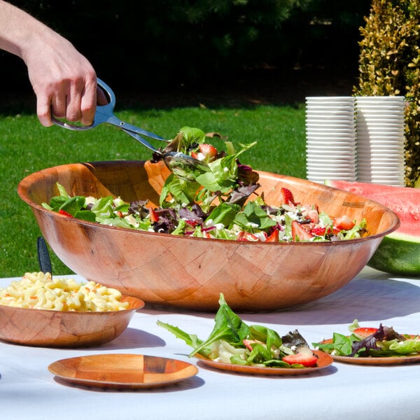 A hand mixing salad in a Thunder Group woven wood bowl on a table with salad and pasta plates.