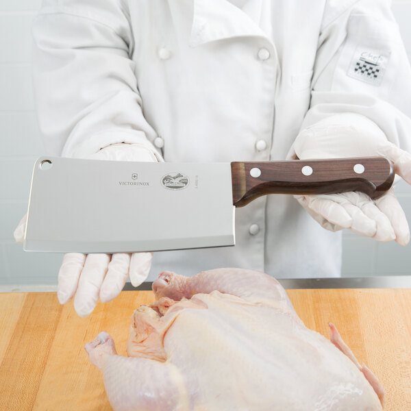 A person with a wooden tray holds a Victorinox cleaver over a raw chicken.