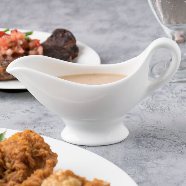 A white Reserve by Libbey bone china gravy boat with sauce in it on a plate of food.