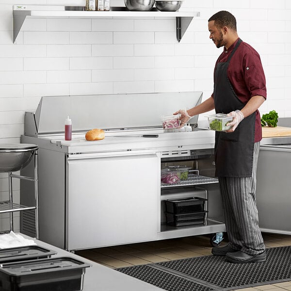 An Avantco 2 door stainless steel refrigerator in a professional kitchen being filled with food in containers by a man in a chef's uniform.