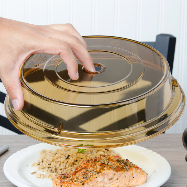 A hand using a Cambro amber low profile plate cover to put a lid on a plate of food.