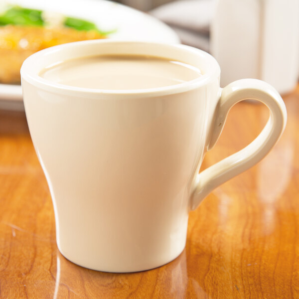 A close-up of a white Elite Global Solutions melamine mug full of coffee on a table.