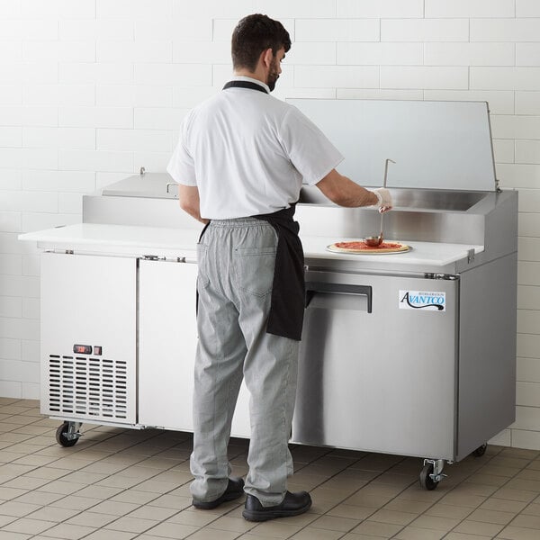 A man in a white shirt and grey pants preparing food on an Avantco refrigerated pizza prep table.